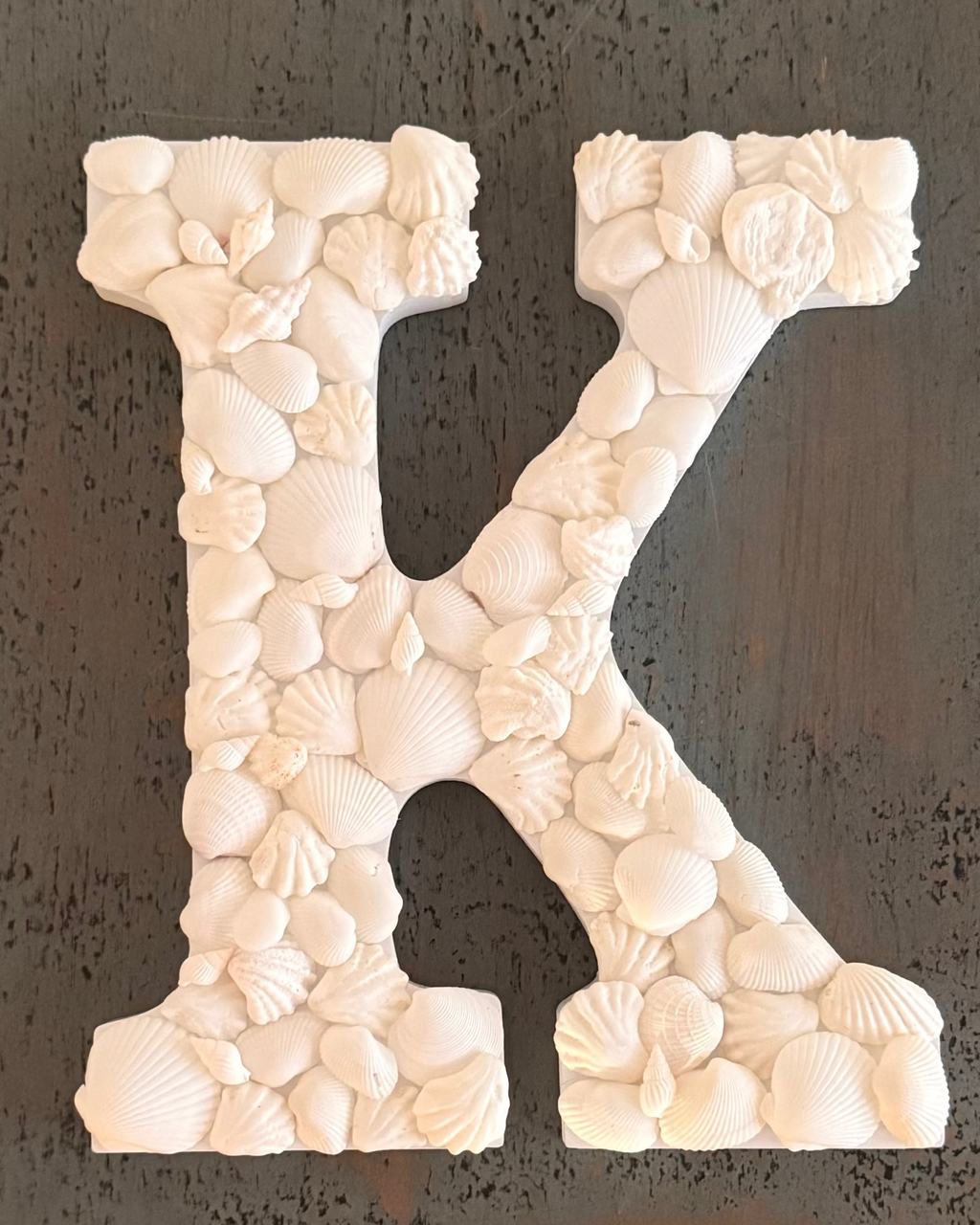 Decorative letter 'K' made of seashells on a dark background