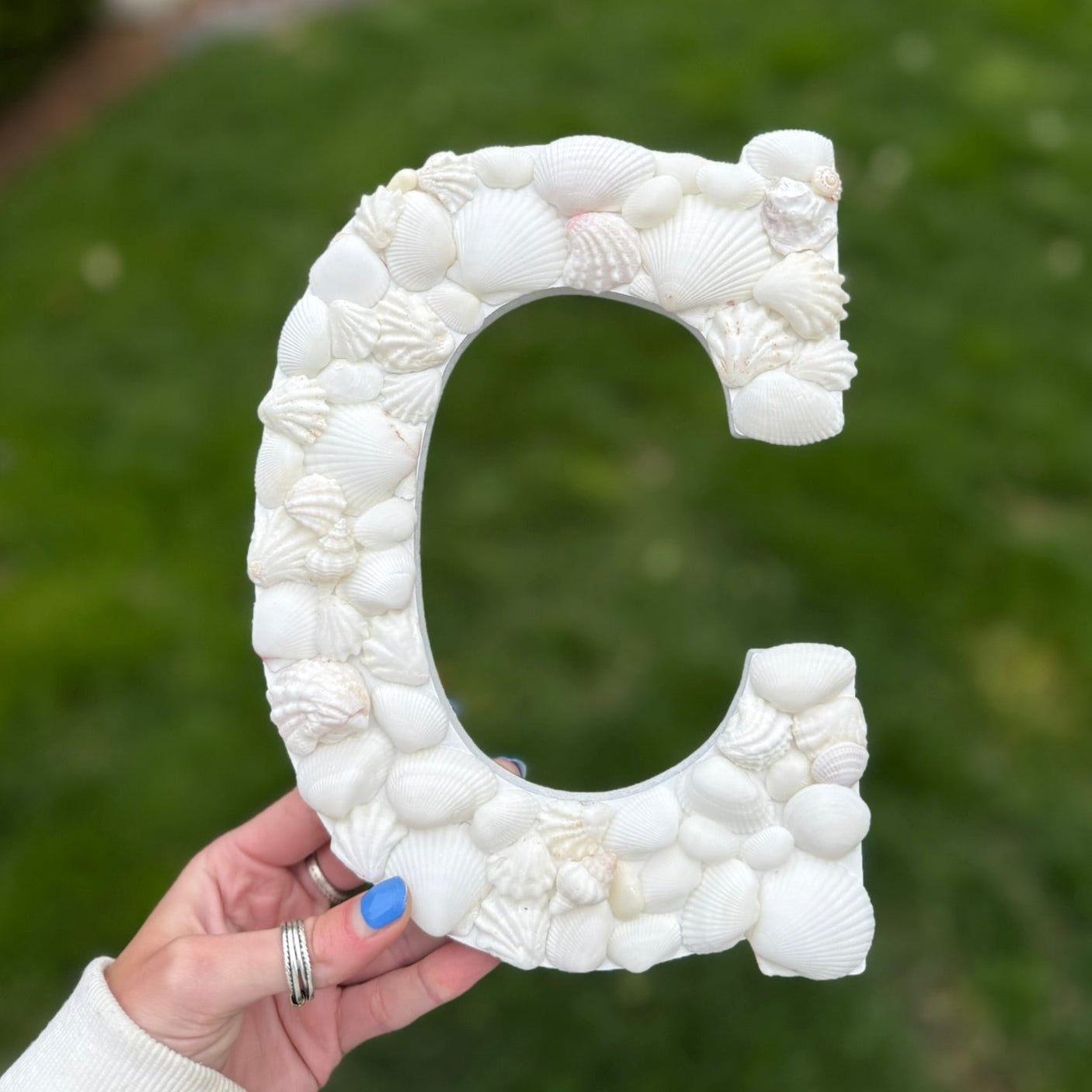 White textured letter 'C' held by a hand with a blurred green outdoor background