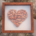 Heart-shaped red coral arrangement in a wooden frame on a textured surface with blurred background