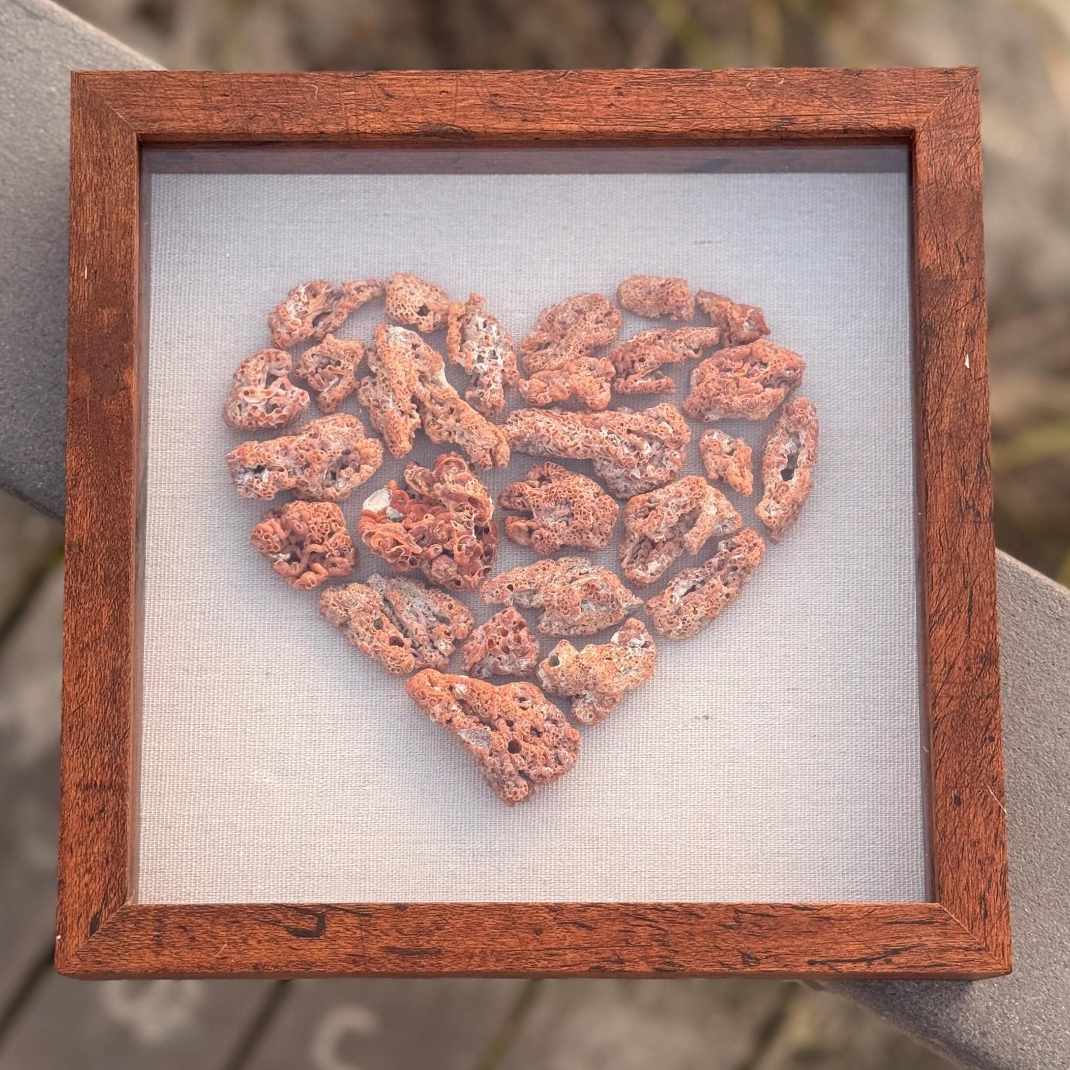 Heart-shaped red coral arrangement in a wooden frame on a textured surface with blurred background