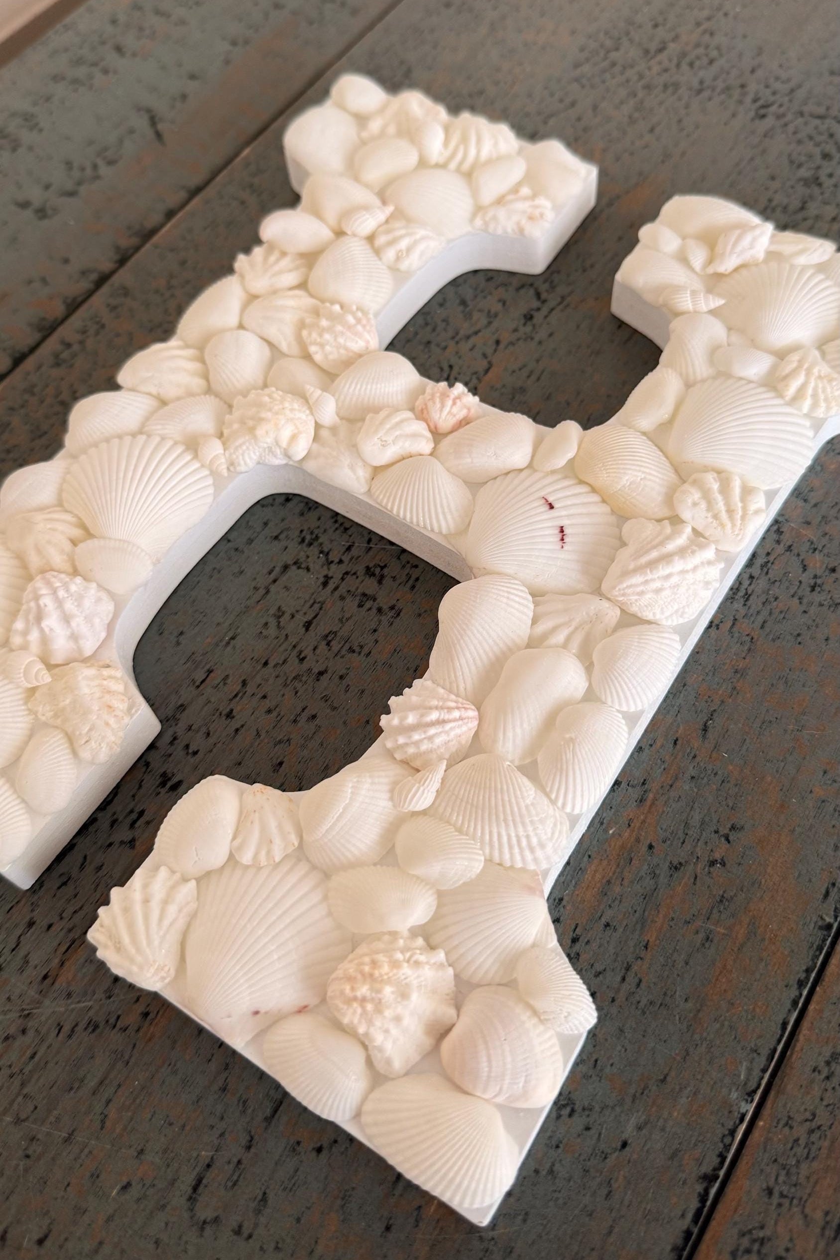 Decorative letter 'H' made of seashells on a dark wooden surface