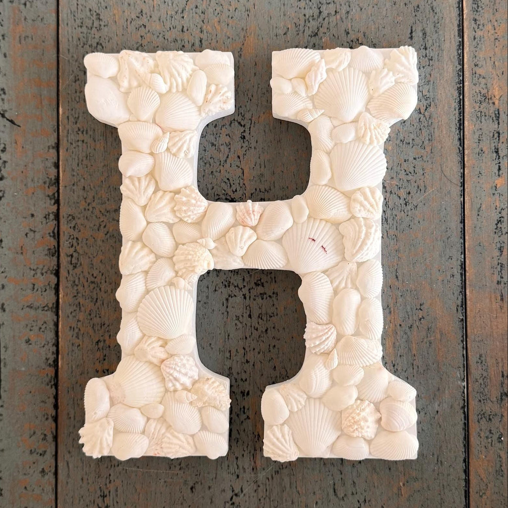 Decorative letter 'H' made of seashells on a wooden background