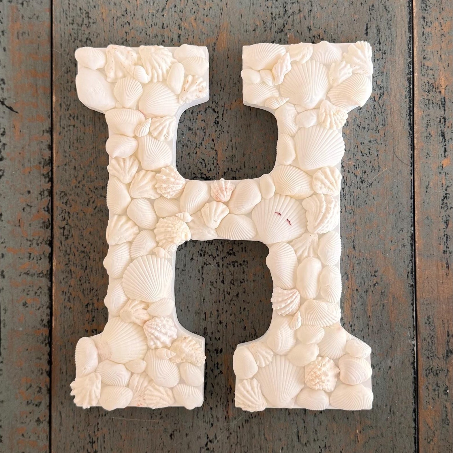 Decorative letter 'H' made of seashells on a wooden background